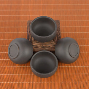 Top view of four Jianshui zitao tea cups with black matte finish, arranged around a wooden stand