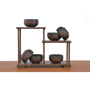 Set of Jianshui zitao tea cups (black) with line-carved floral patterns, displayed on a tiered wooden stand