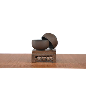 Two Jianshui zitao teacups in a warm brown tone with a bodhi leaf–inspired texture, displayed on a carved wooden stand