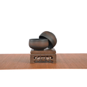 Two small Jianshui zitao tea cups with chattering-carved texture, stacked on a wooden display stand