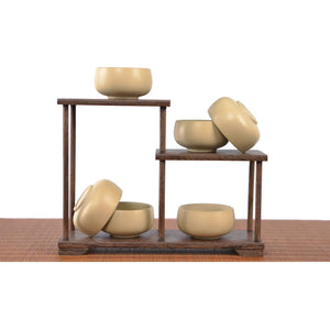 Six light-toned Jianshui zitao teacups displayed on a wooden stand, featuring minimalist unglazed forms with a smooth matte finish