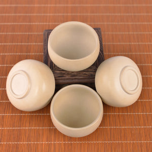 Four small Two small light-toned Jianshui zitao teacups stacked on a carved wooden stand, featuring a smooth unglazed matte finish and minimalist design
