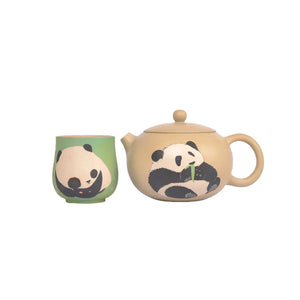 A beige Jianshui zitao teapot, decorated with a panda design, sits next to a matching green teacup, which is engraved with a different image of a panda
