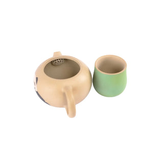 Top-down view of a beige Jianshui zitao teapot with built-in filter holes, shown alongside a green matching cup