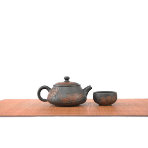 Handmade pottery Shi Piao teapot with a line-carved lotus design, displayed with one matching tea cup.