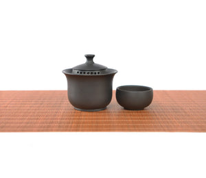 Handcrafted black pottery gaiwan set with finger-grip lid and built-in filter holes, featuring a minimalist tea bowl and matching cup.