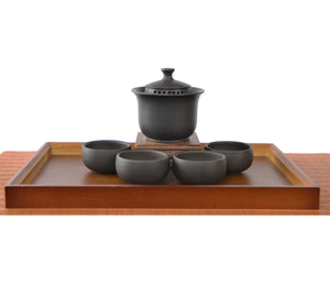 Handcrafted black pottery gaiwan set with finger-grip lid and built-in filter holes, displayed with four matching tea cups.