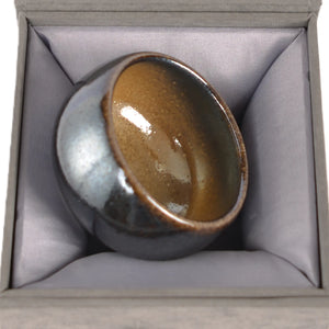 Handcrafted wood-fired teacup resting in a presentation box, featuring a glossy natural ash glaze interior and unglazed exterior with organic kiln-fired textures