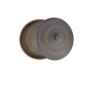 Handmade pottery tea cake storage box shown open, with the lid set aside to reveal the smooth unglazed interior; the lid features a raised knob and a circular band of hand-carved jump-cut texture on a dark matte surface.