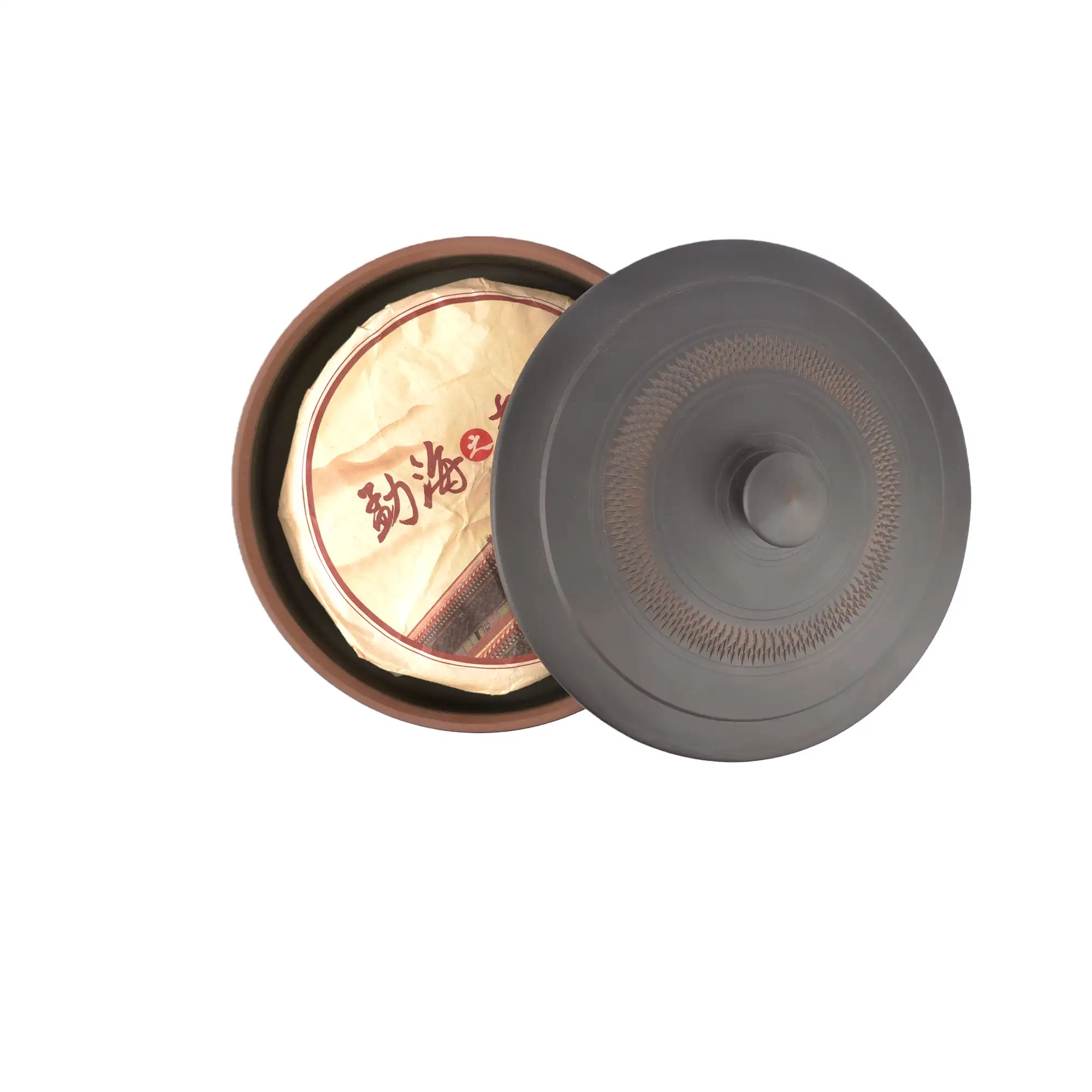 Handmade pottery tea cake storage box shown open with the lid set aside, revealing a compressed tea cake inside; the lid features a carved jumping-knife pattern,.
