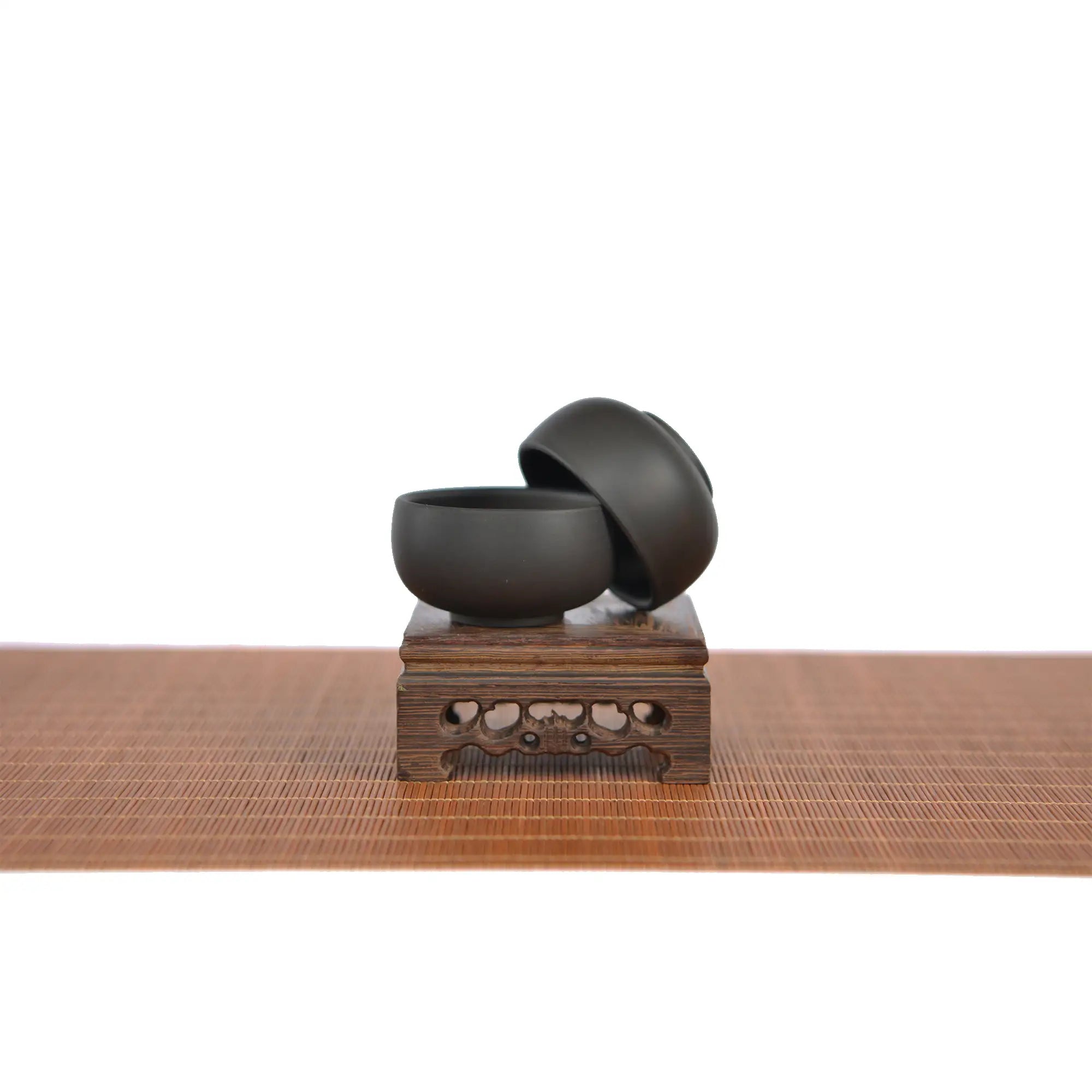 Two handcrafted Jianshui zitao tea cups with a matte black finish, displayed on a carved wooden stand