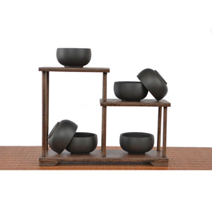 Six Jianshui zitao tea cups with a matte black finish on a tiered wooden stand