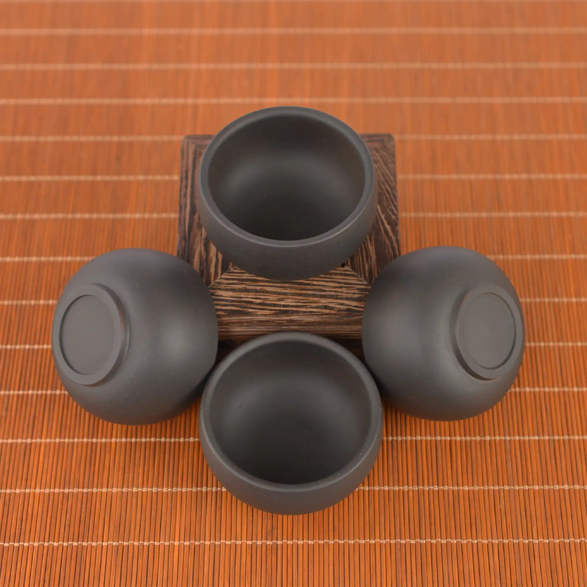 Top view of four Jianshui zitao tea cups with black matte finish, arranged around a wooden stand