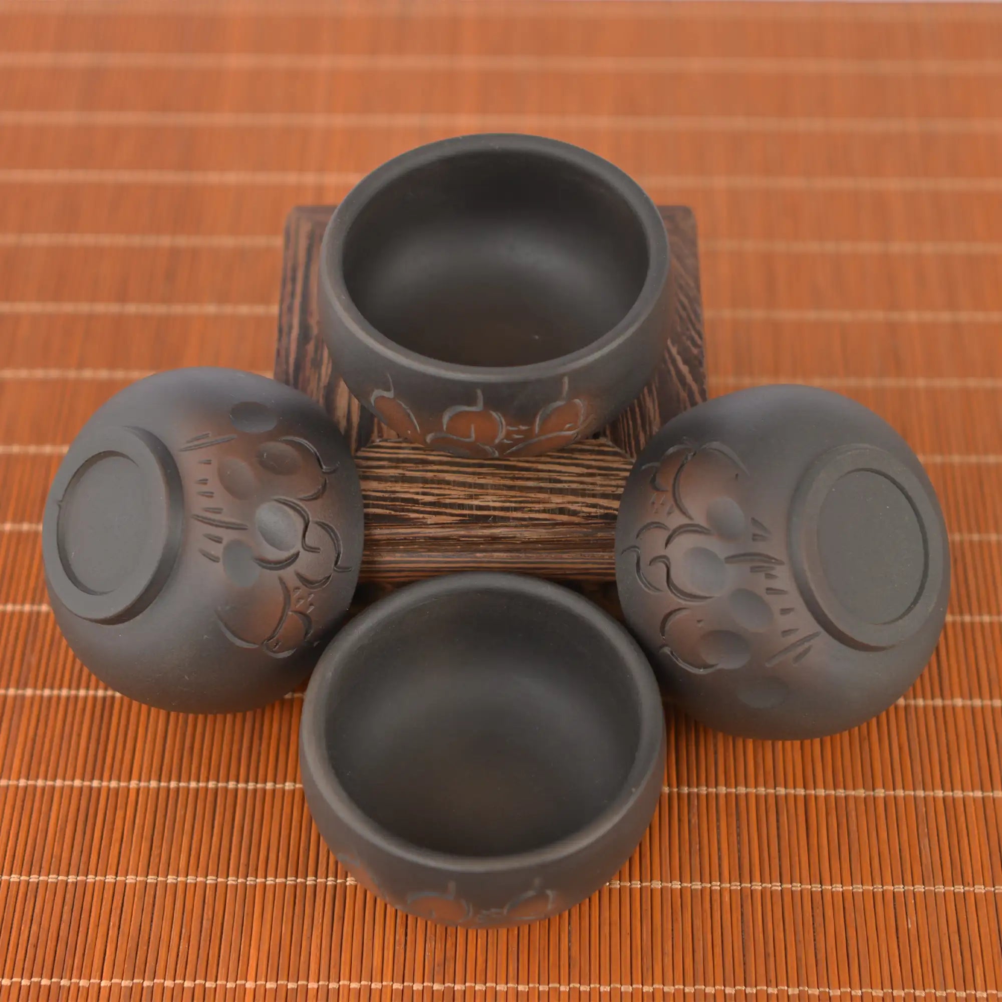 Top view of four Jianshui zitao tea cups (black) with line-carved floral patterns, arranged around a wooden stand