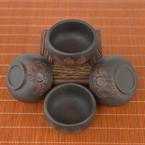 Top view of four Jianshui zitao tea cups (black) with line-carved floral patterns, arranged around a wooden stand