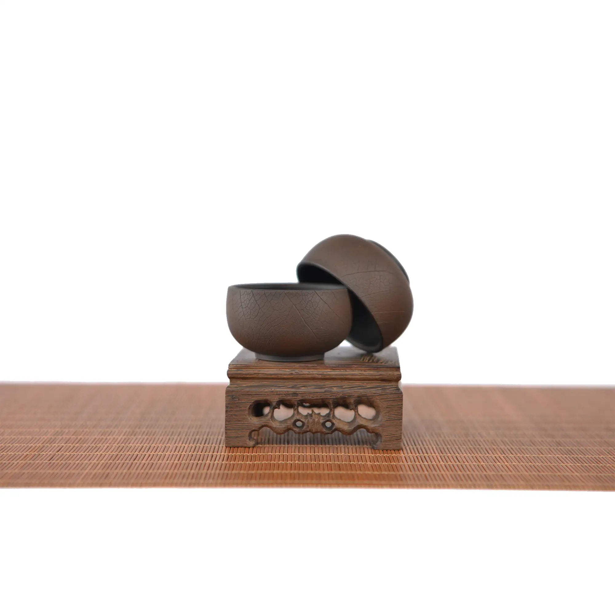 Two Jianshui zitao teacups in a warm brown tone with a bodhi leaf–inspired texture, displayed on a carved wooden stand