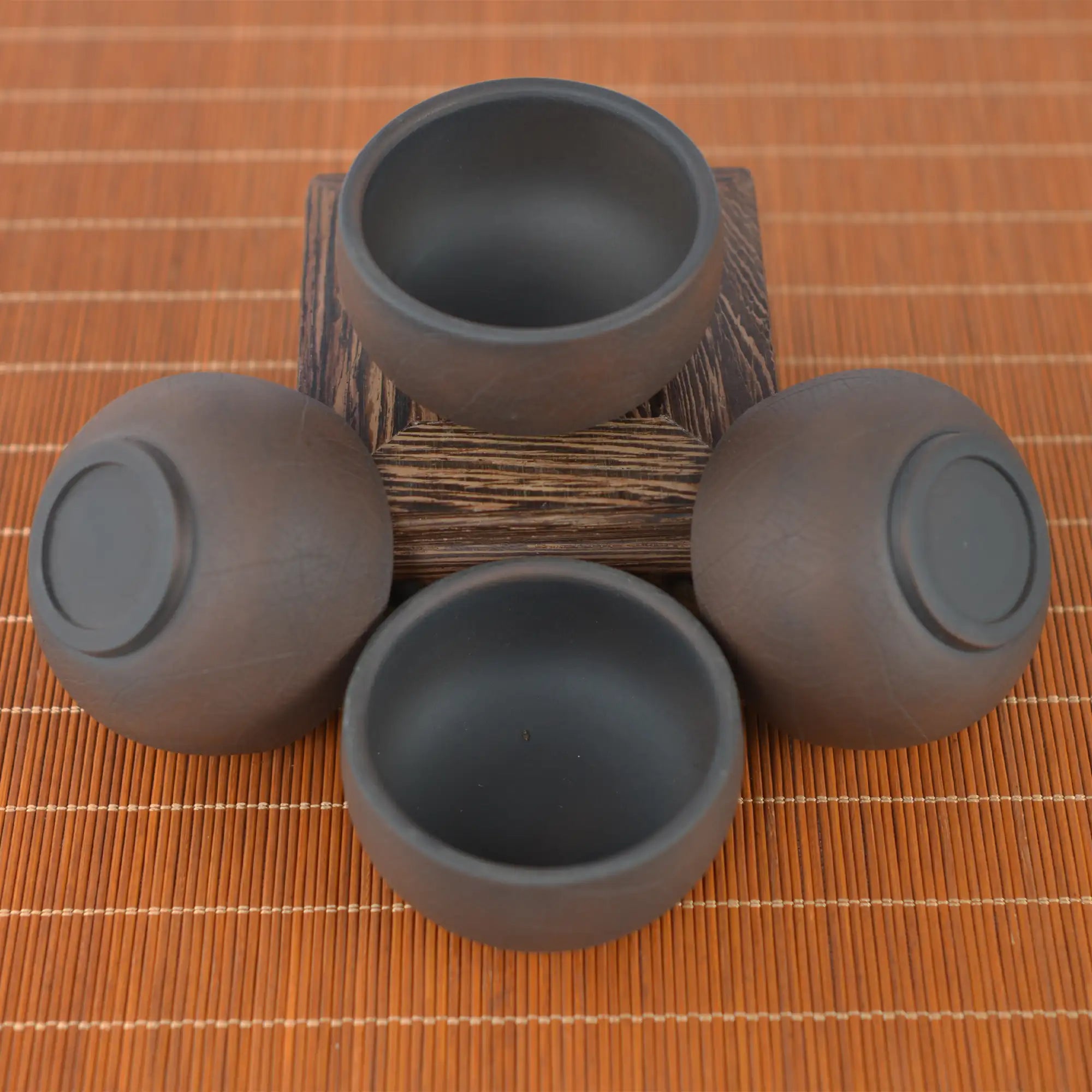 Top view of four Jianshui zitao tea cups warm brown tone with a bodhi-leaf–inspired texture, arranged around a wooden stand