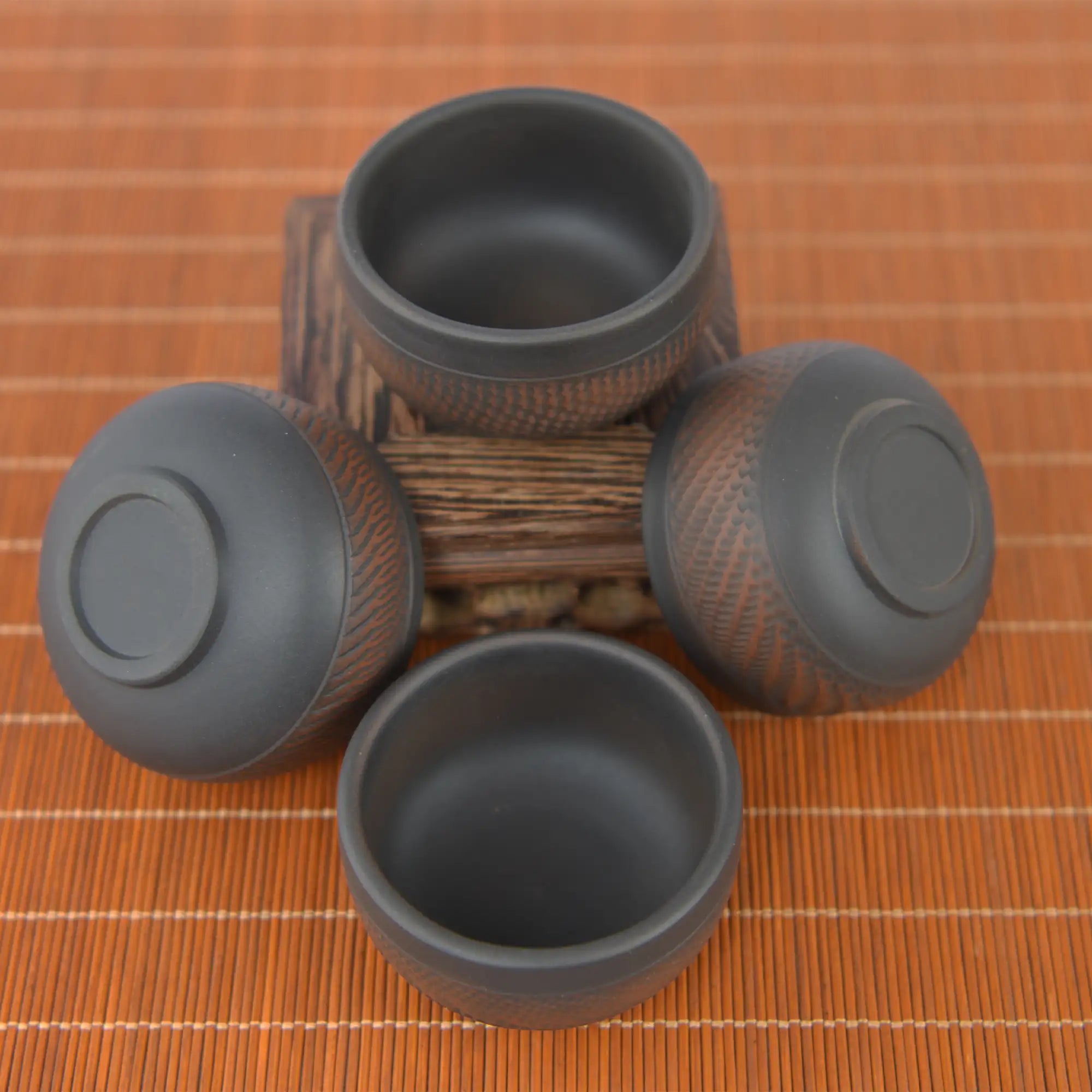 Four small Jianshui zitao tea cups with chattering-carved texture, displayed from multiple angles on a wooden stand