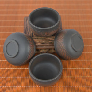 Four small Jianshui zitao tea cups with chattering-carved texture, displayed from multiple angles on a wooden stand