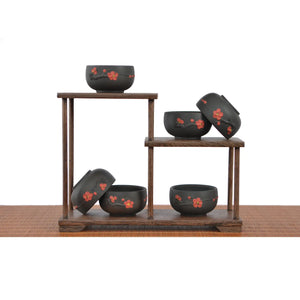 Six Jianshui zitao tea cups with red plum blossom design displayed on a tiered wooden stand