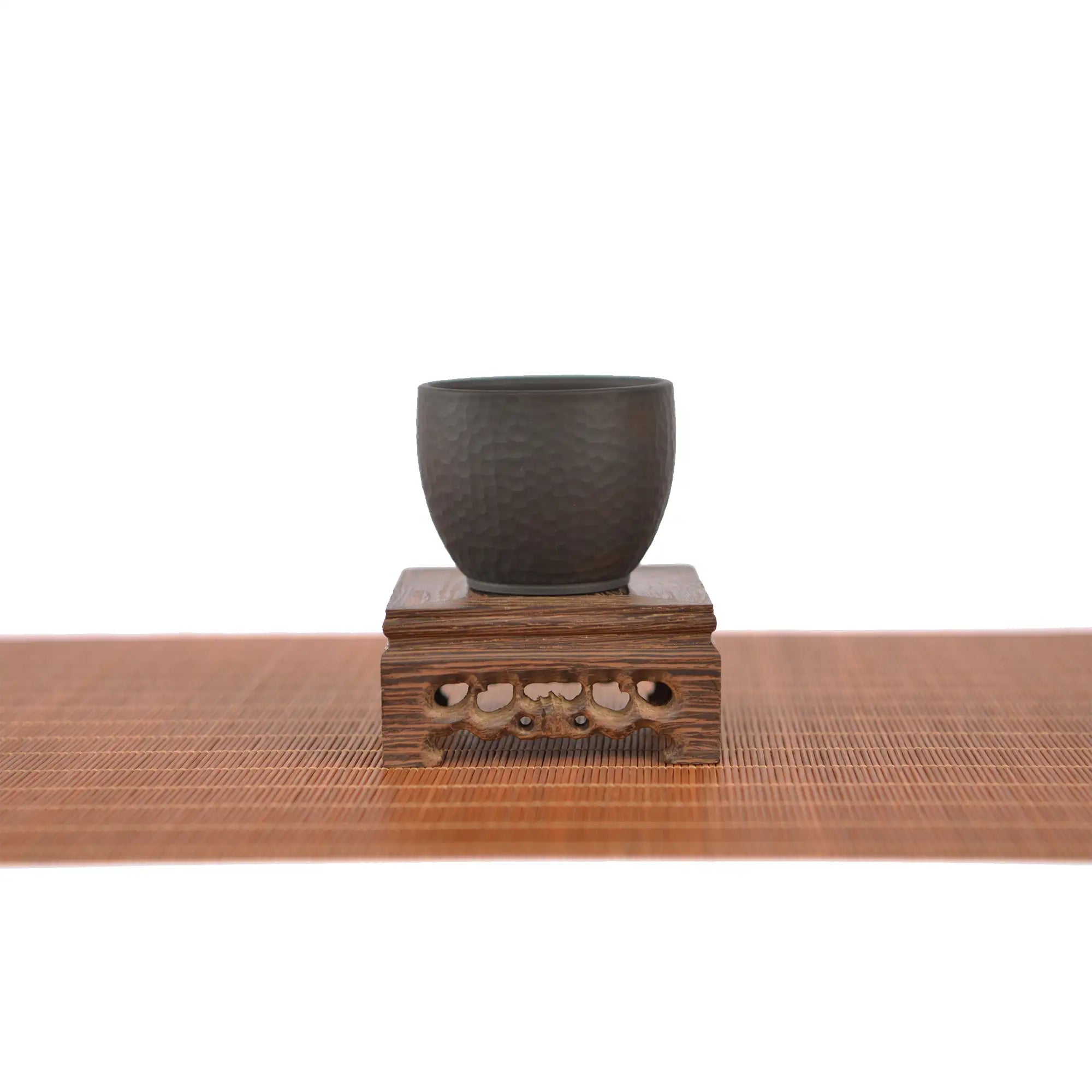 Jianshui zitao dark clay master tea cup displayed on a carved wooden stand, highlighting its hammer-textured surface and matte unglazed finish