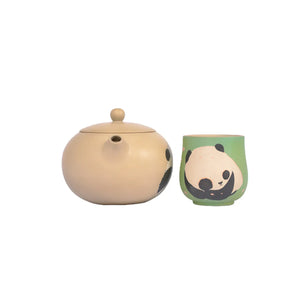 A handcrafted Jianshui zitao teapot, decorated with a panda pattern, sits next to a matching green teacup featuring a different panda design