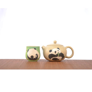 A set of handcrafted Jianshui zitao teapots and green teacups, decorated with hand-engraved panda motifs, sits on a woven mat