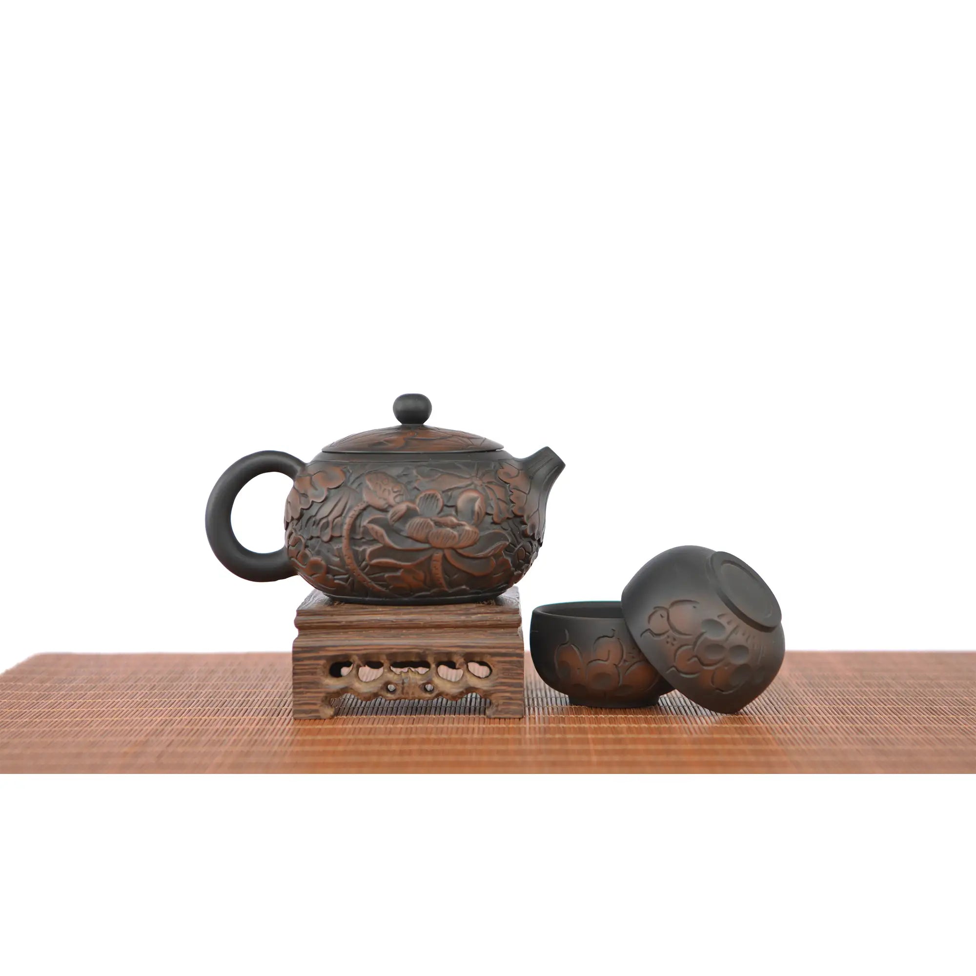 Jianshui zitao teapot with fully carved lotus design, displayed on a wooden stand with two matching tea cups