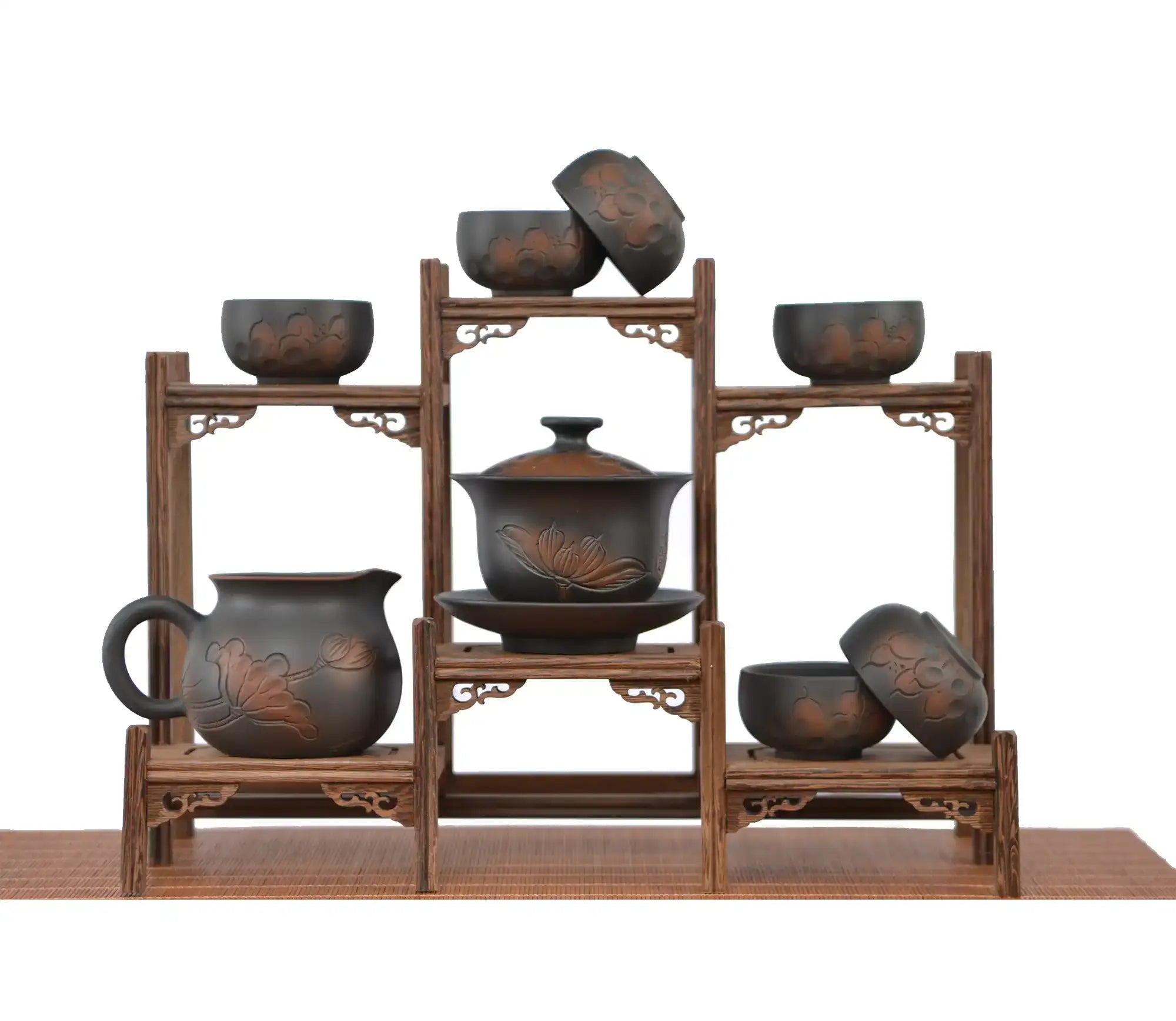 Complete hand-carved lotus tea set displayed on a tiered wooden stand, featuring a lotus-engraved gaiwan at the center, a matching fairness pitcher, and multiple dark clay teacups with carved lotus patterns arranged above and below.