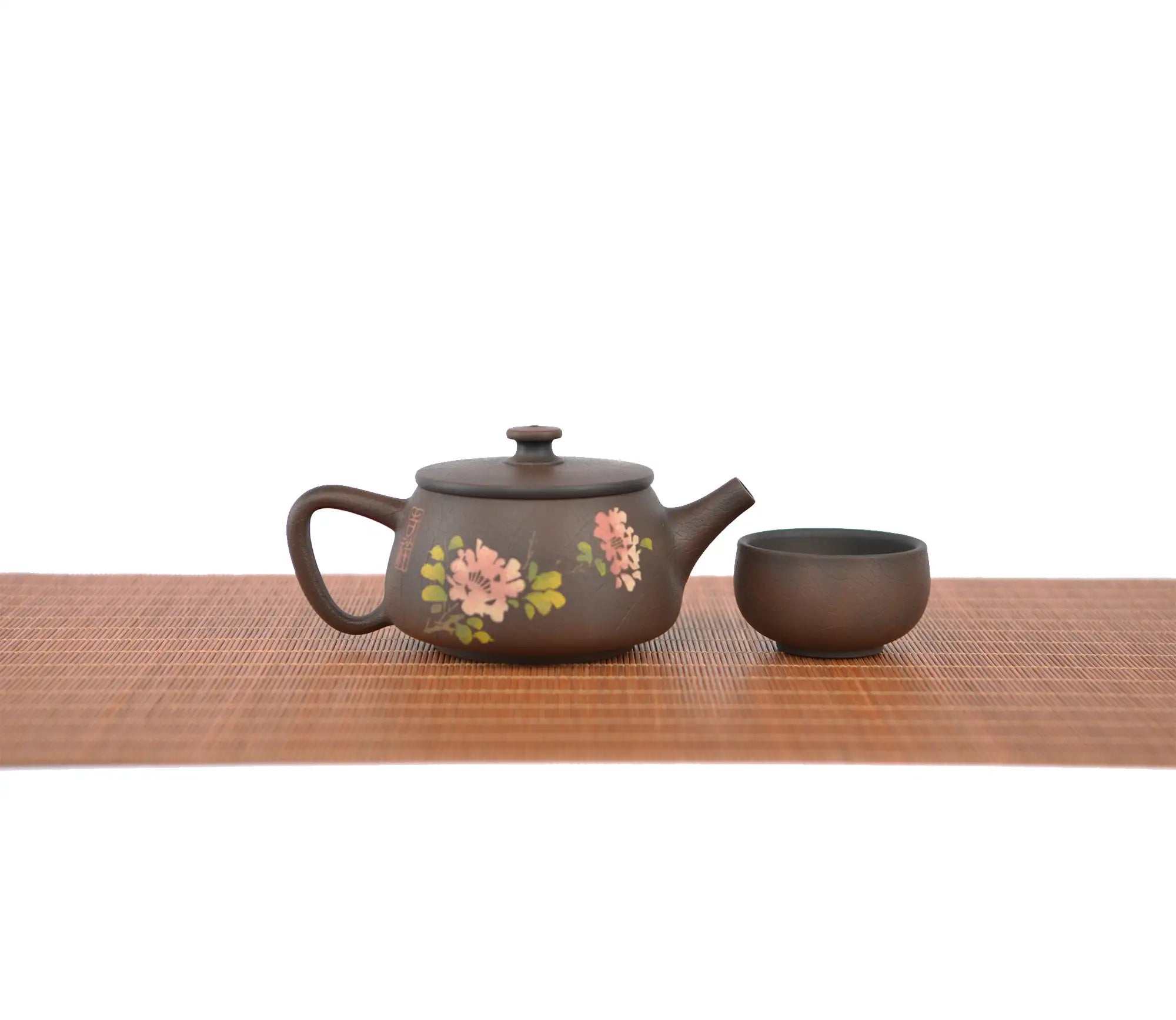 Handcrafted unglazed pottery teapot with a Bodhi-style crackle texture and engraved peony floral design, shown with a matching teacup on a woven mat.
