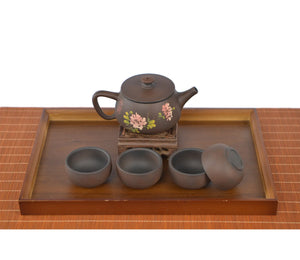Handcrafted unglazed pottery teapot with a Bodhi-style crackle texture and engraved peony design, displayed with four matching teacups on a wooden tray.