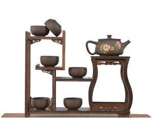 Handcrafted unglazed pottery teapot with a Bodhi-style crackle texture and engraved peony floral motif, displayed with six matching teacups on a tiered wooden display stand.