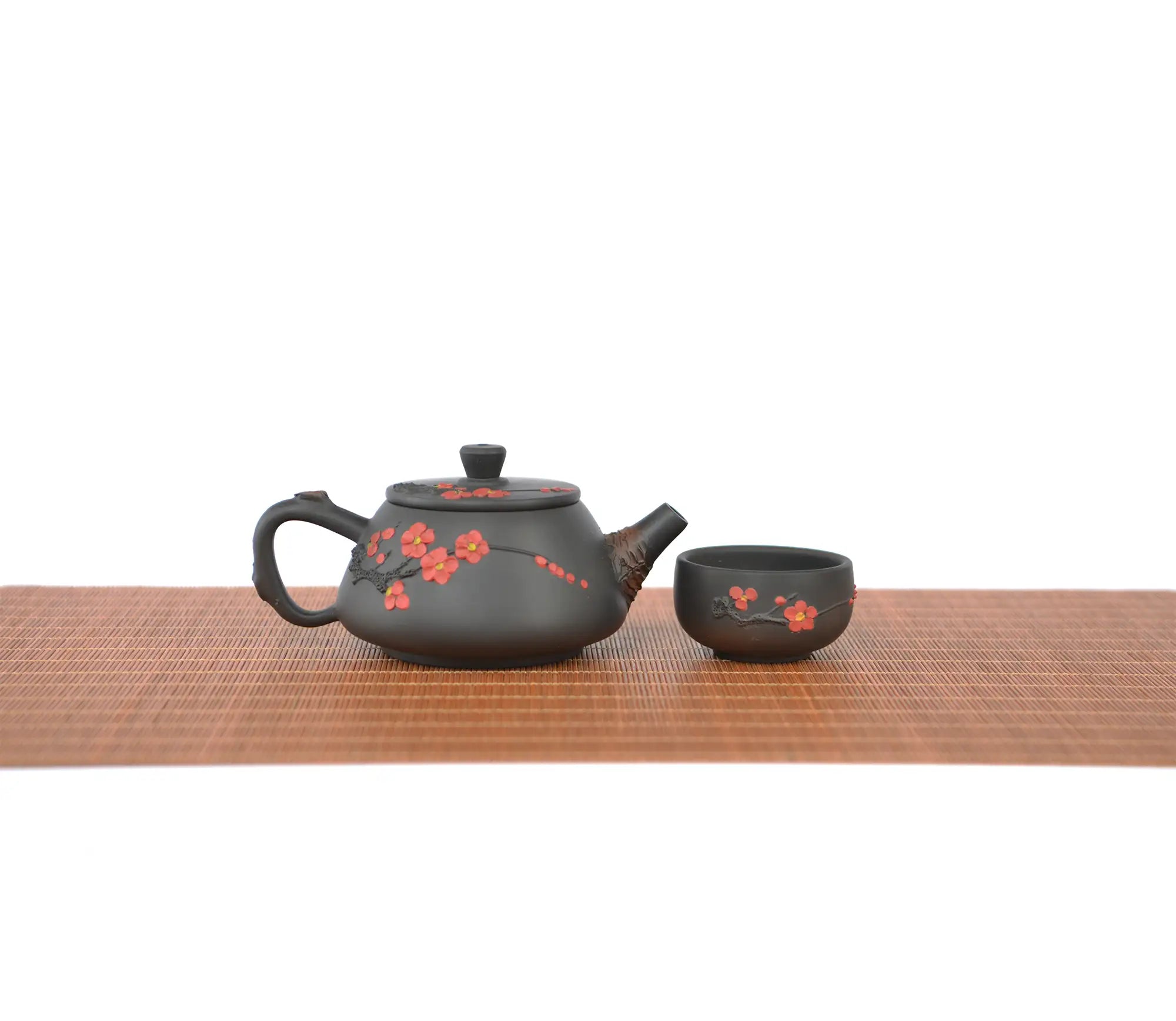 Handcrafted Jianshui zitao root-carved unglazed teapot with plum blossom  , paired with a matching teacup on a woven tea mat