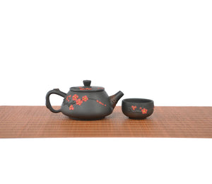 Handcrafted Jianshui zitao root-carved unglazed teapot with plum blossom  , paired with a matching teacup on a woven tea mat