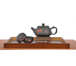 Jianshui zitao root-carved unglazed teapot with a smooth matte finish and plum blossom, displayed with two matching teacups on a wooden tea tray and carved stand