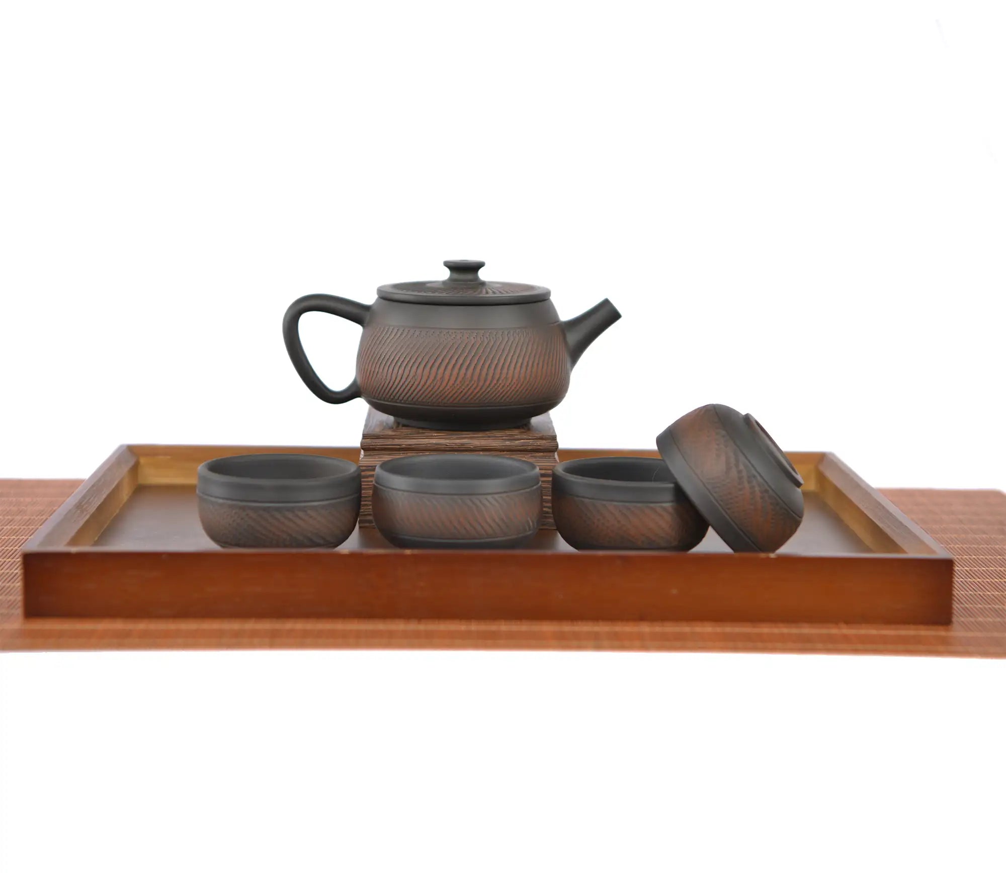 Handcrafted pottery teapot with a chattered knife  texture and unglazed matte finish, arranged with four matching teacups on a wooden tea tray.