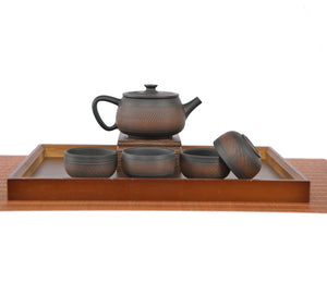 Handcrafted pottery teapot with a chattered knife  texture and unglazed matte finish, arranged with four matching teacups on a wooden tea tray.