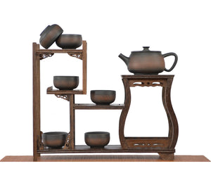 Handcrafted chattered-texture pottery teapot with an unglazed matte finish, displayed with multiple matching teacups on a tiered wooden tea display stand.