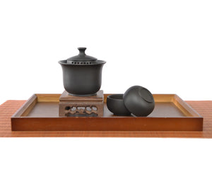 Handcrafted black pottery gaiwan set with finger-grip lid and built-in filter holes, displayed with two matching tea cups.