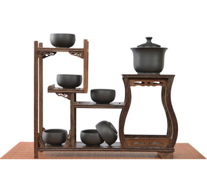 Handcrafted black pottery gaiwan tea set with finger-grip lid and built-in filter holes, displayed with six matching cups on a wooden tea stand.